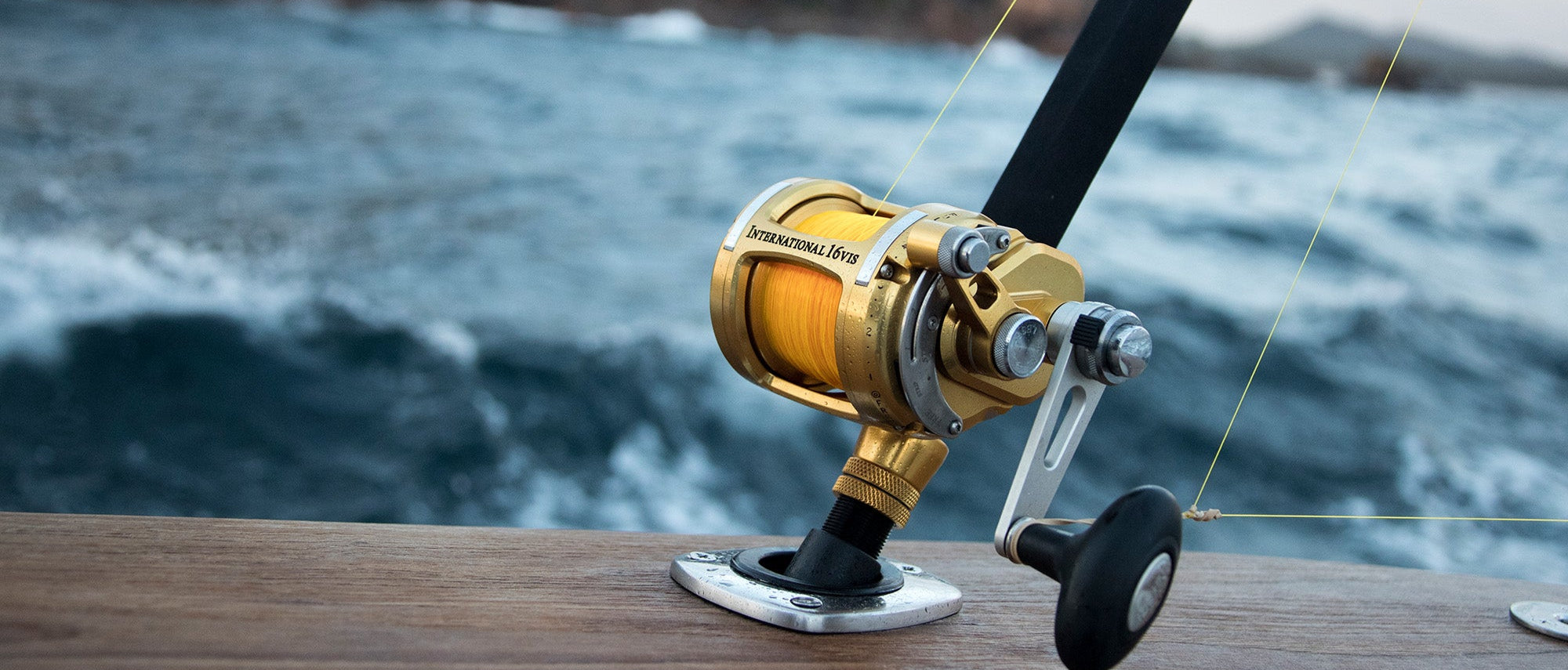 Fishing reel on a wooden surface with water in the background