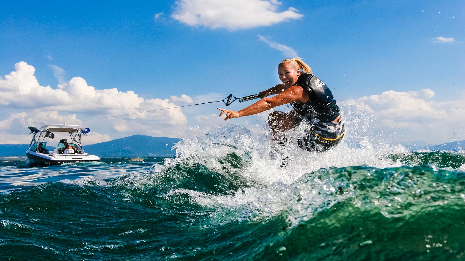 Person wakeboarding on a wave with a boat in the background